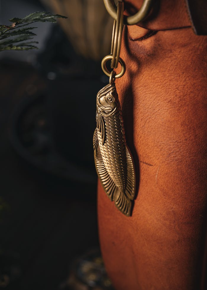 Elegant handmade brass fish keychain attached to a leather bag, perfect for gifts.