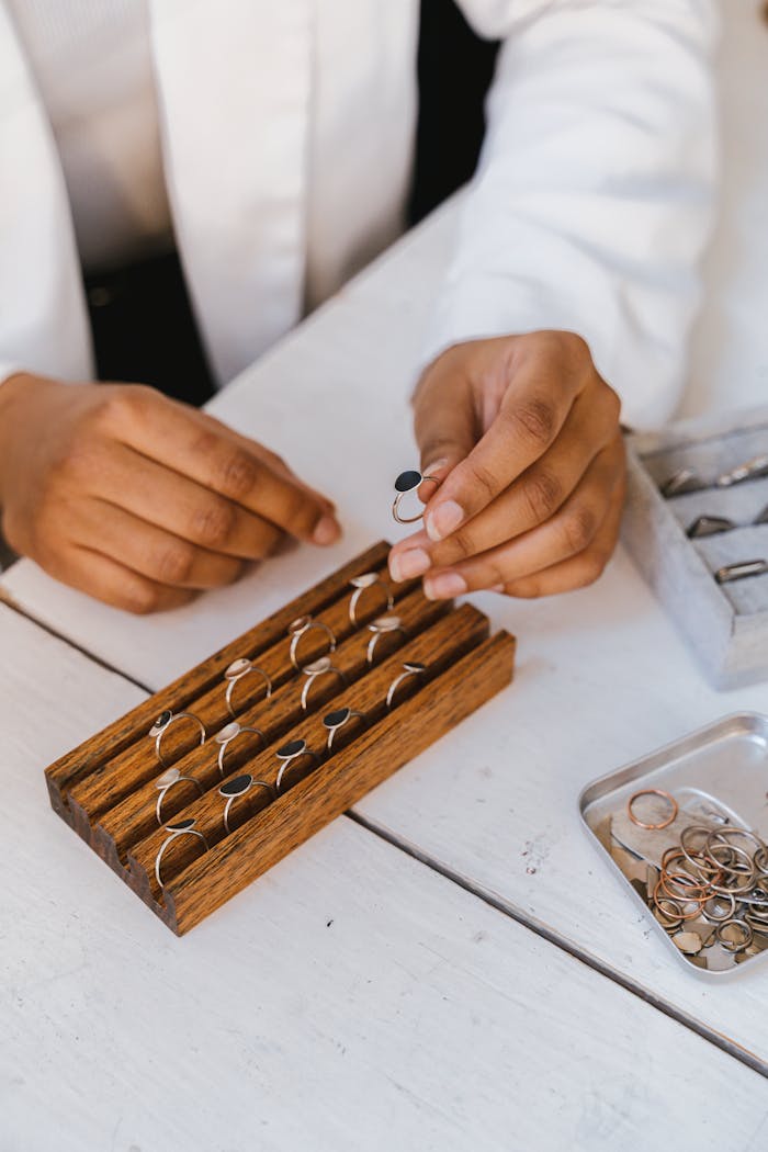 Close-up of hands arranging rings in a wooden display box, showcasing jewelry organization.